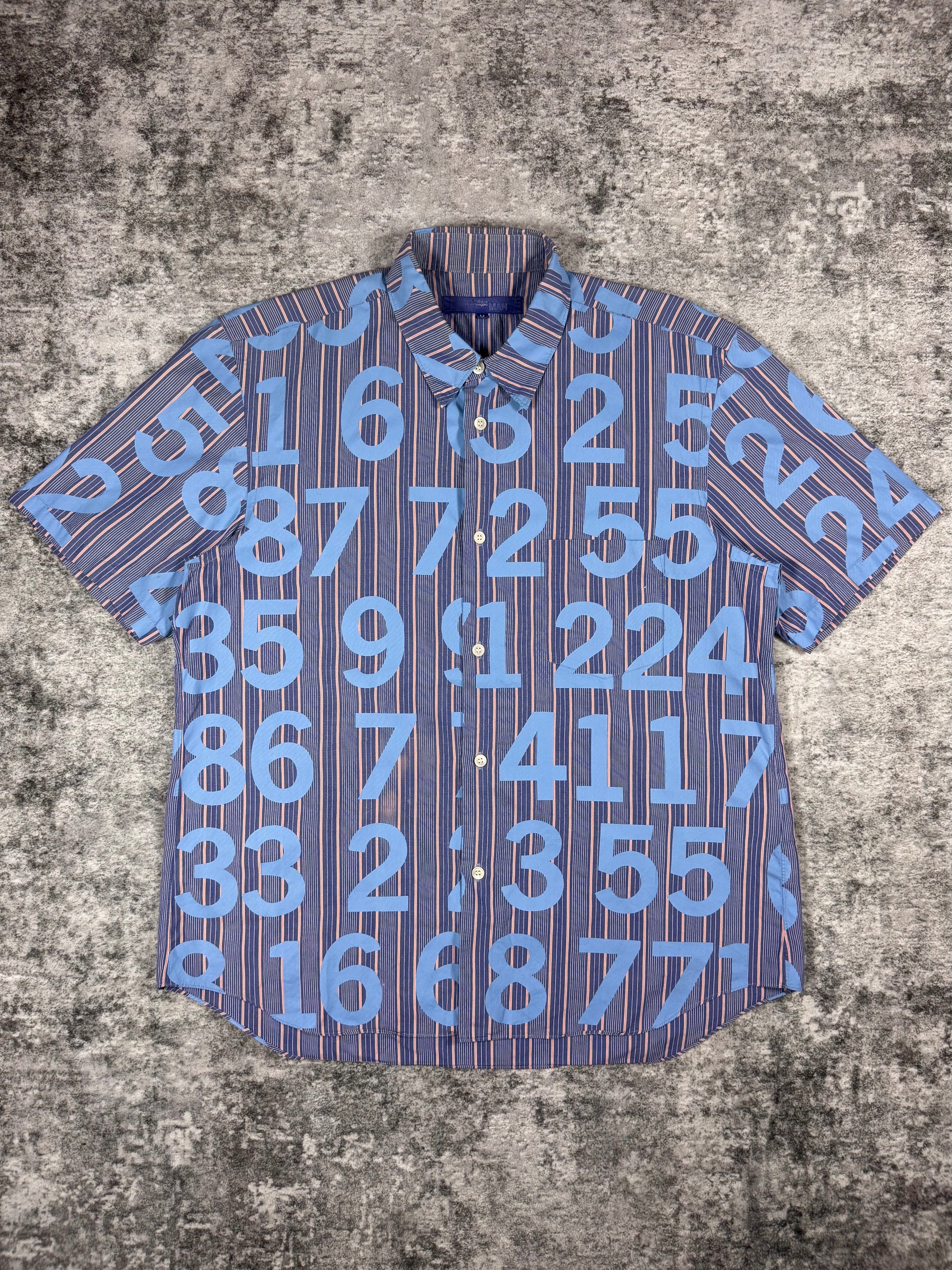 SS03 Junya Watanabe Comme des Garçons Man short-sleeve button-up shirt featuring all-over numeric print, photographed flat on a textured grey surface.