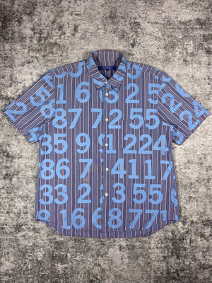 SS03 Junya Watanabe Comme des Garçons Man short-sleeve button-up shirt featuring all-over numeric print, photographed flat on a textured grey surface.