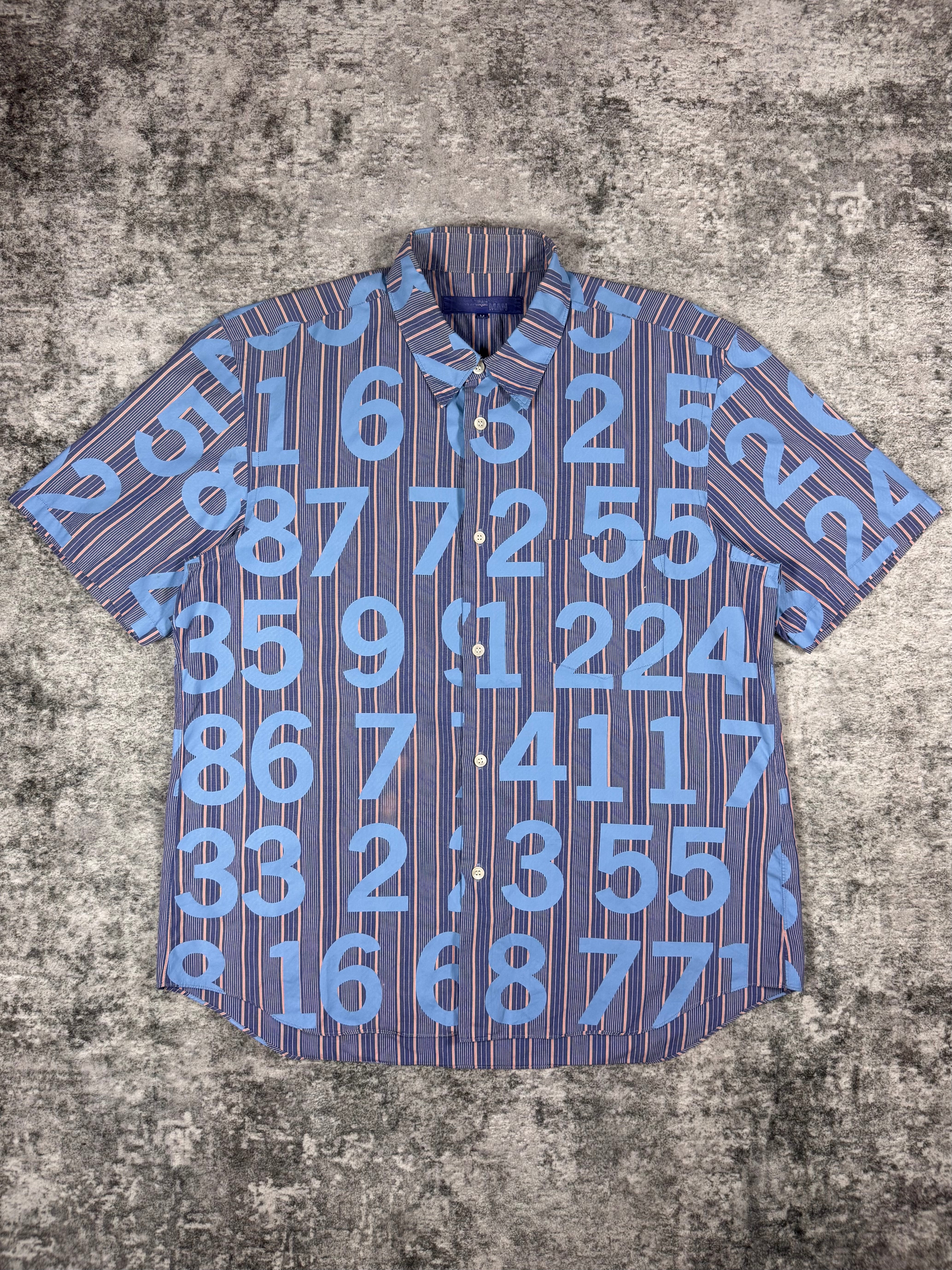 SS03 Junya Watanabe Comme des Garçons Man short-sleeve button-up shirt featuring all-over numeric print, photographed flat on a textured grey surface.