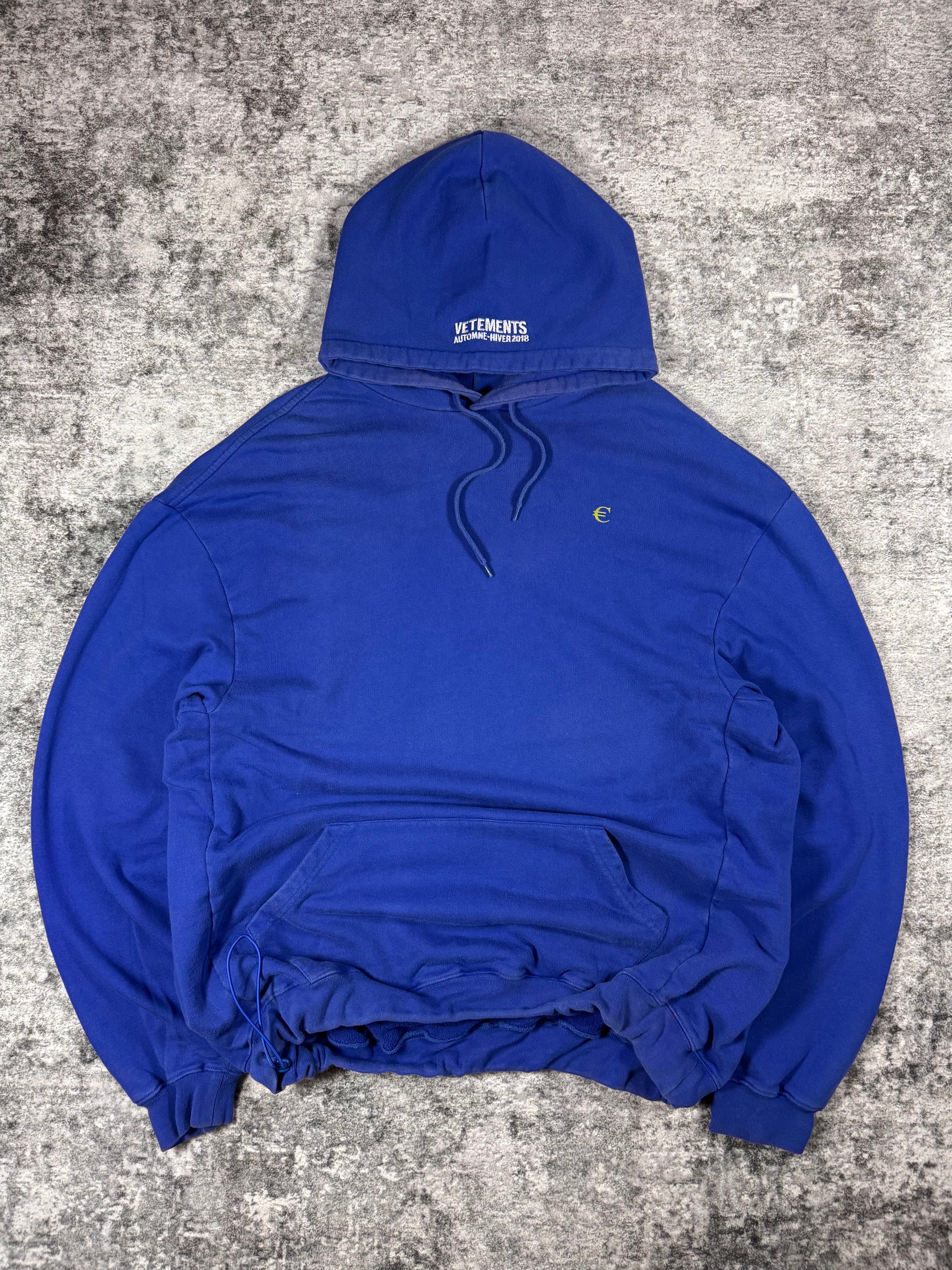 Royal blue Vetements Fall/Winter 2018 European Union hoodie laid flat, featuring circle of yellow EU stars printed on the back, small euro symbol embroidery on the chest, oversized fit, and adjustable bungee cord hem.