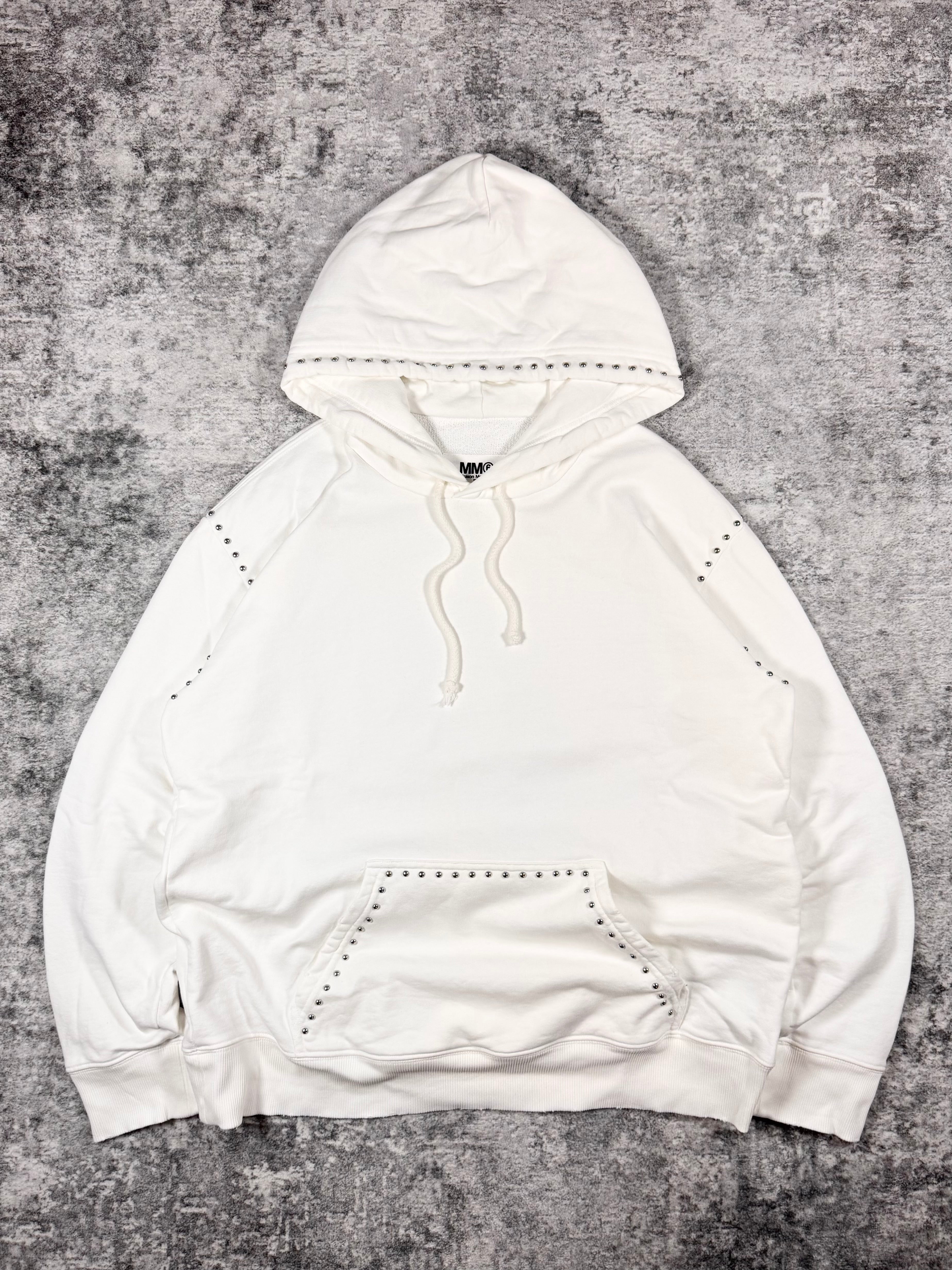 FW22 Maison Margiela MM6 white cotton hoodie featuring metal stud trim along the hood, sleeves, and kangaroo pocket, photographed flat on a grey textured background.