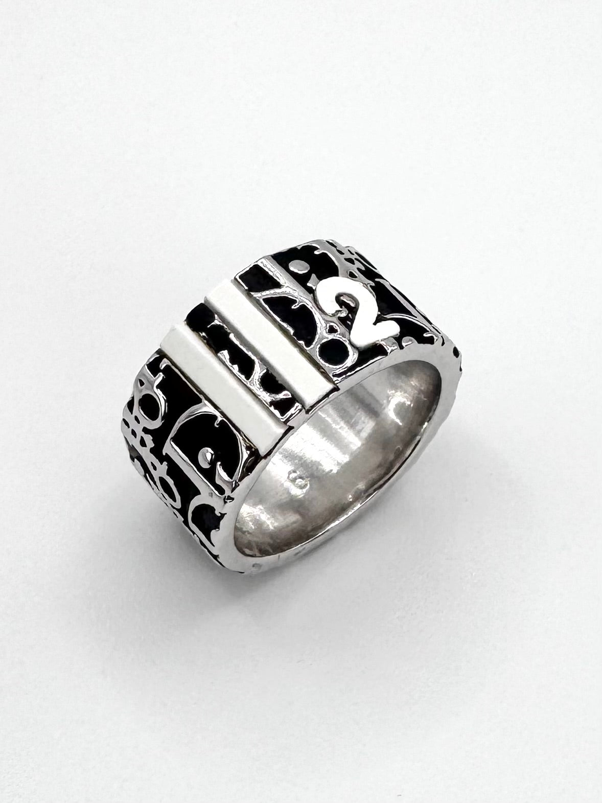 Close-up of Christian Dior Trotter monogram wide band ring with black enamel logo pattern on silver-tone metal.