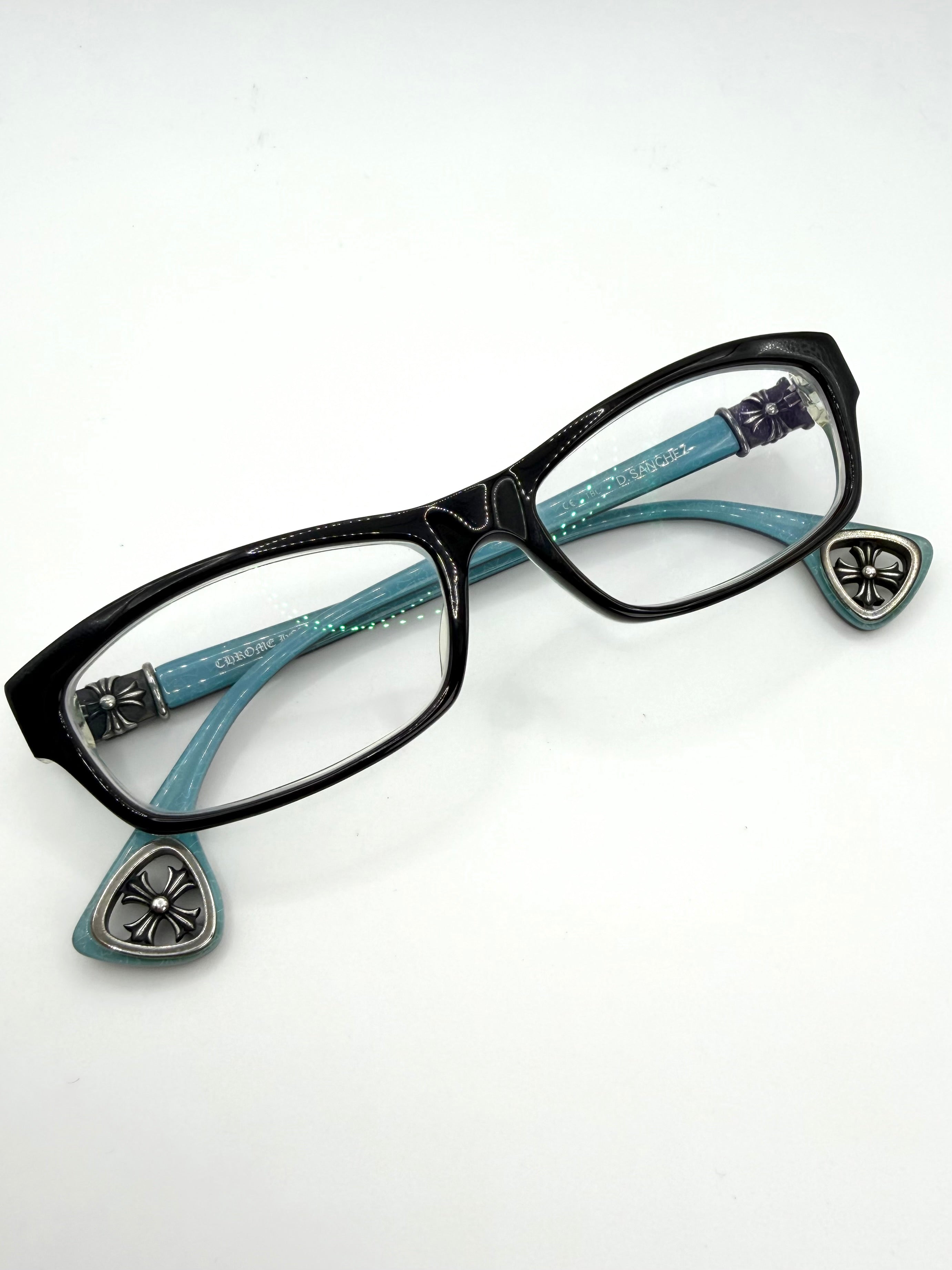 Black chrome hearts d Sanchez cat-eye eyeglasses with turquoise blue temples featuring silver-tone decorative metal crosses and cut-out cross temple tips, shown on a plain white background.