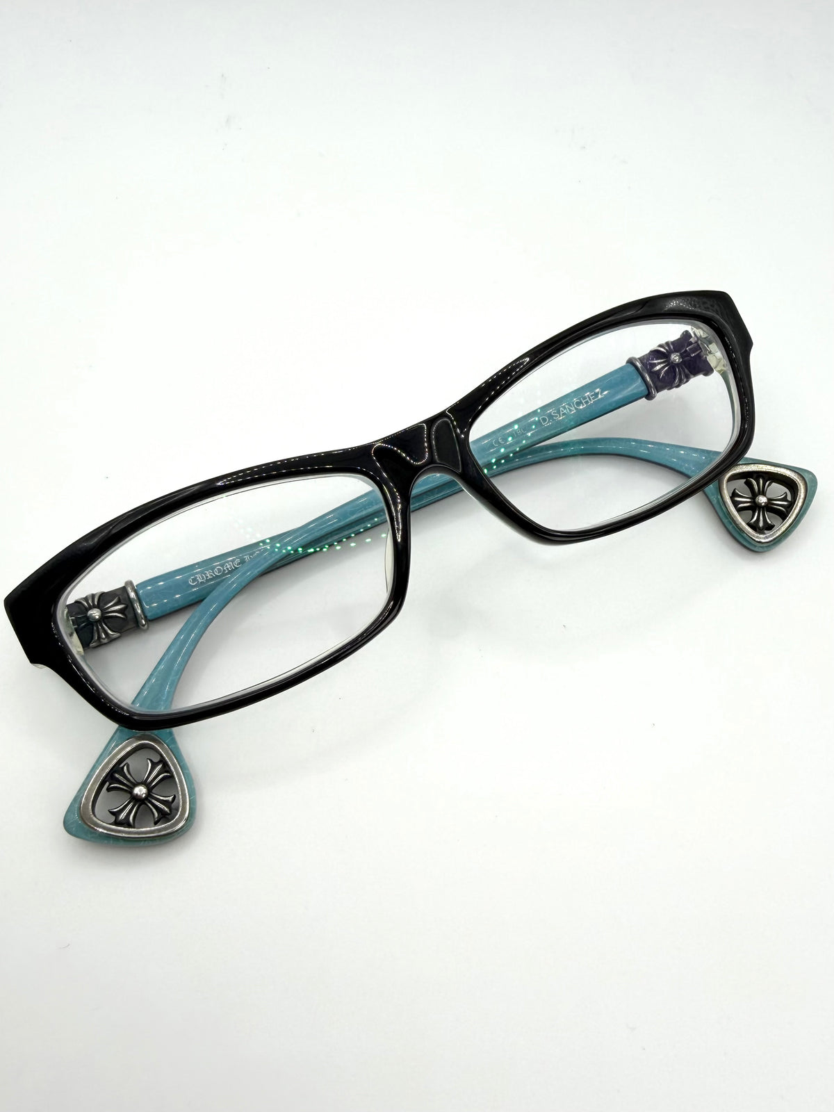 Black chrome hearts d Sanchez cat-eye eyeglasses with turquoise blue temples featuring silver-tone decorative metal crosses and cut-out cross temple tips, shown on a plain white background.