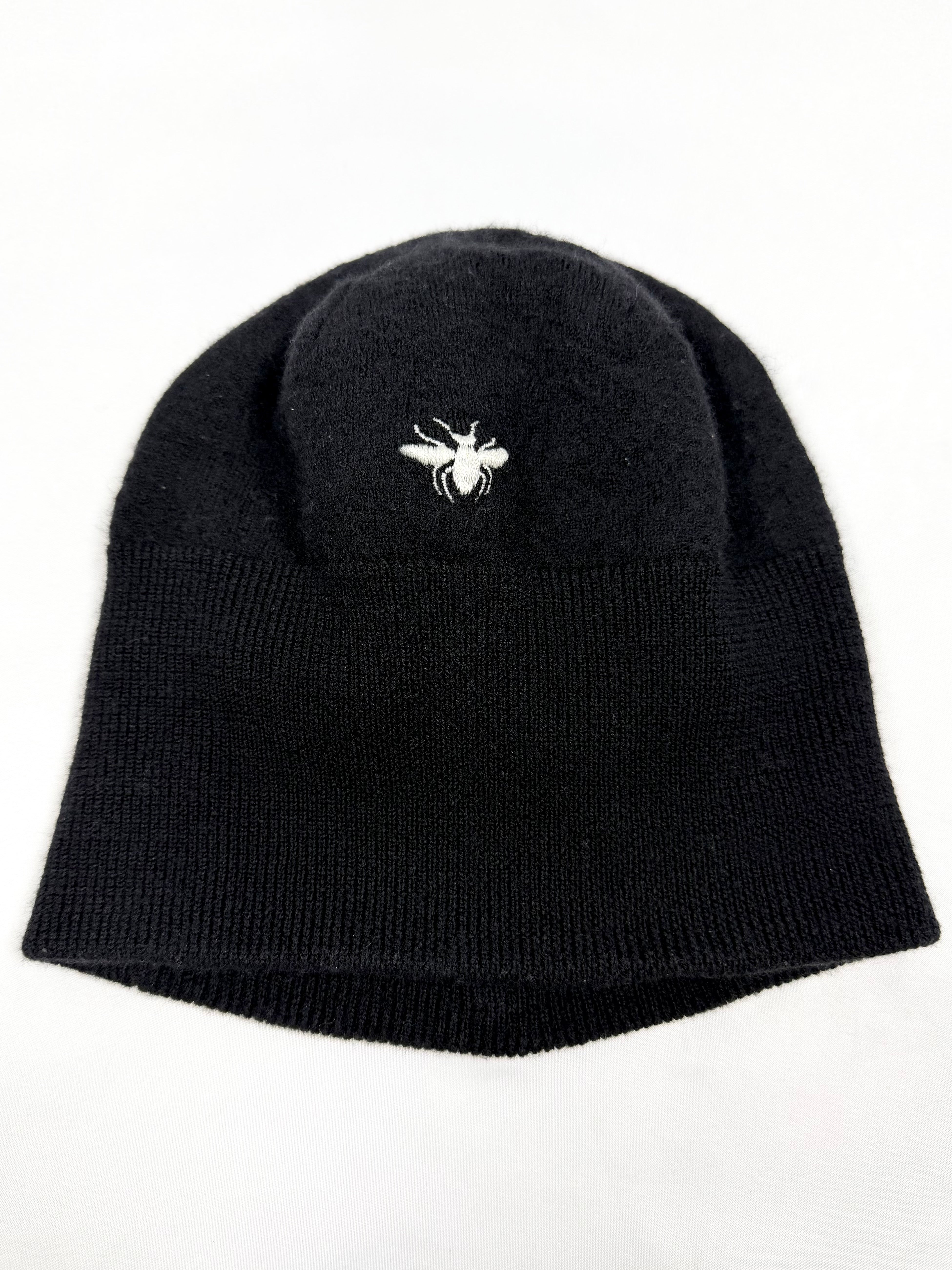 Black Dior Homme These Grey Days Bee Embroidery Beanie with a white bee logo on the ground laid on a white background