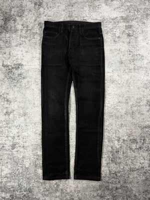 Black Dior Homme jeans with waxed detailing designed by Kris Van Assche on a textured gray carpet