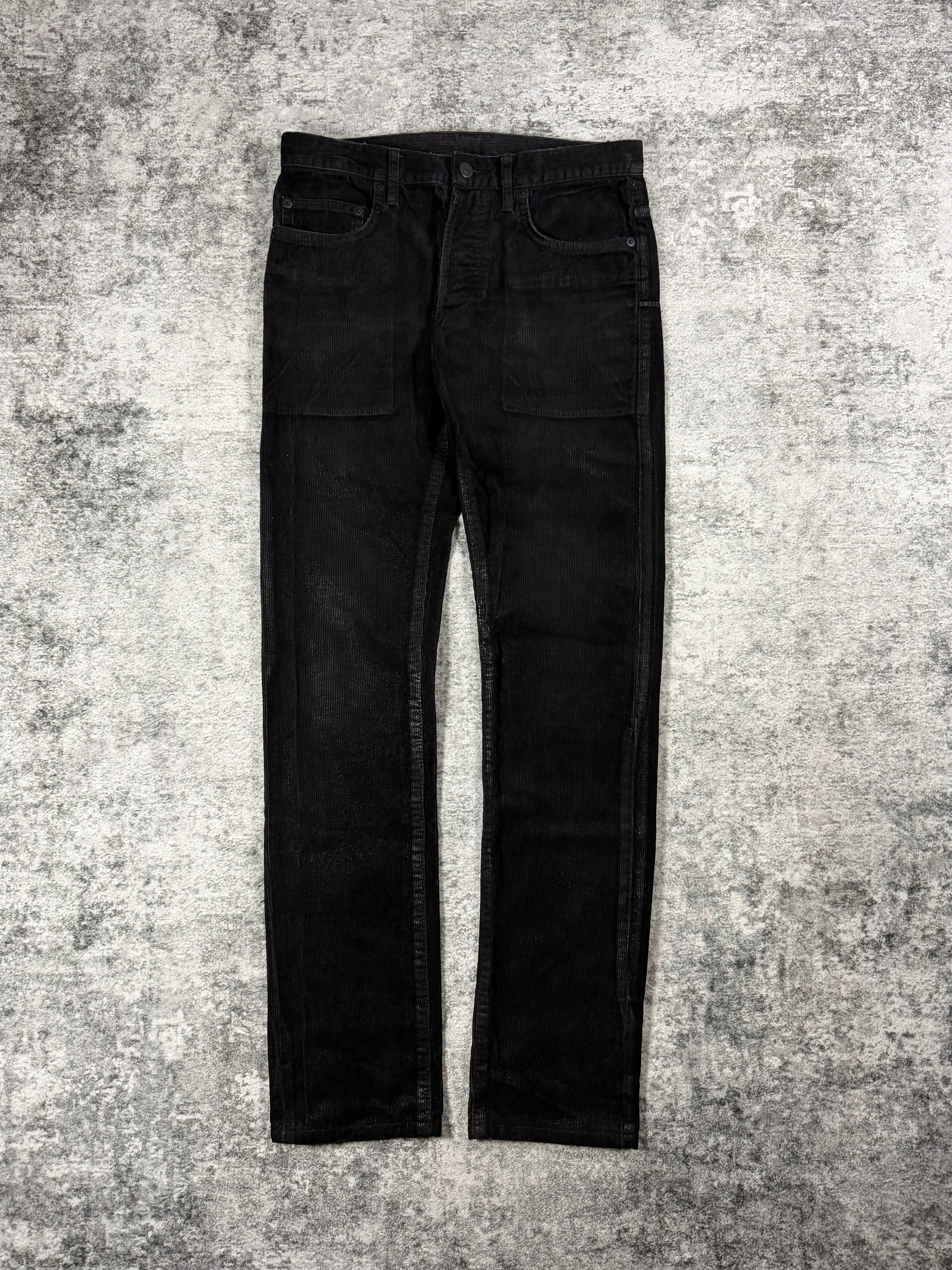 Black Dior Homme jeans with waxed detailing designed by Kris Van Assche on a textured gray carpet