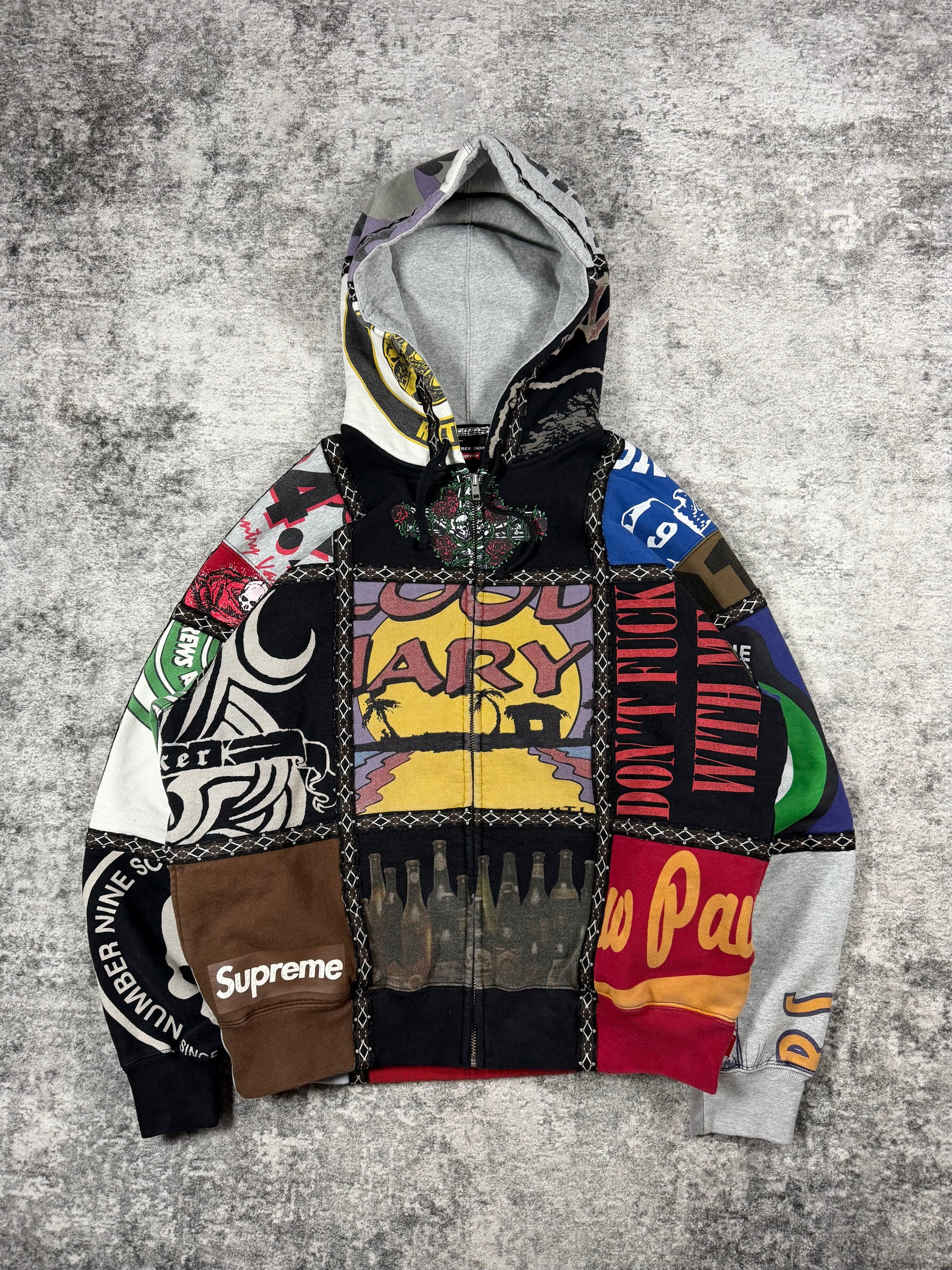 FW25 Number (N)ine x Supreme patchwork zip-up hoodie featuring reconstructed multi-panel graphic fleece construction with assorted logos, skull motifs, typography prints, contrast stitched trim, full zip closure, and hood.