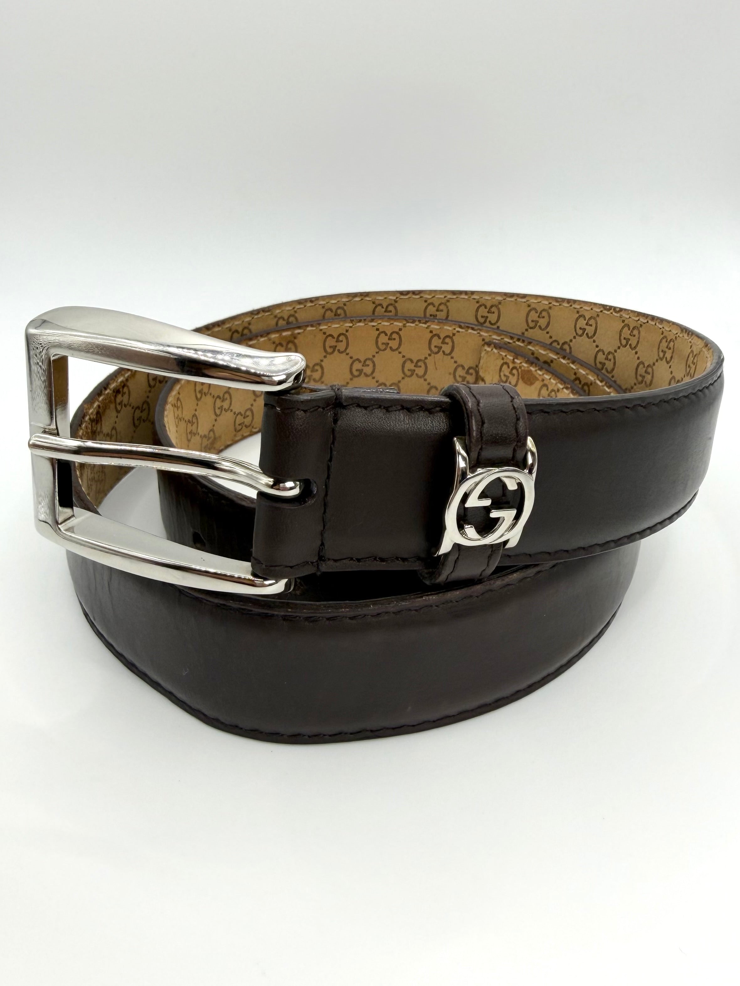 Black Gucci leather belt with a monogram interior and silver buckle with mini GG logo on a white background