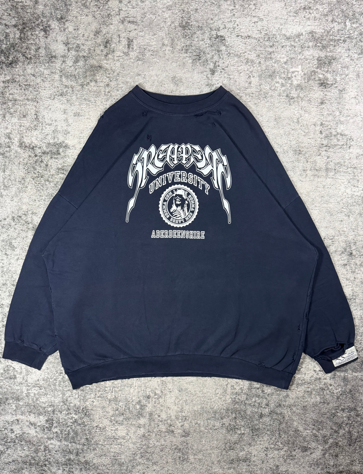 Raf Simons ‘Sreapers University’ Oversized Distress Crewneck from 2022 featuring collegiate inspired logo with a skeleton laid on a grey carpet