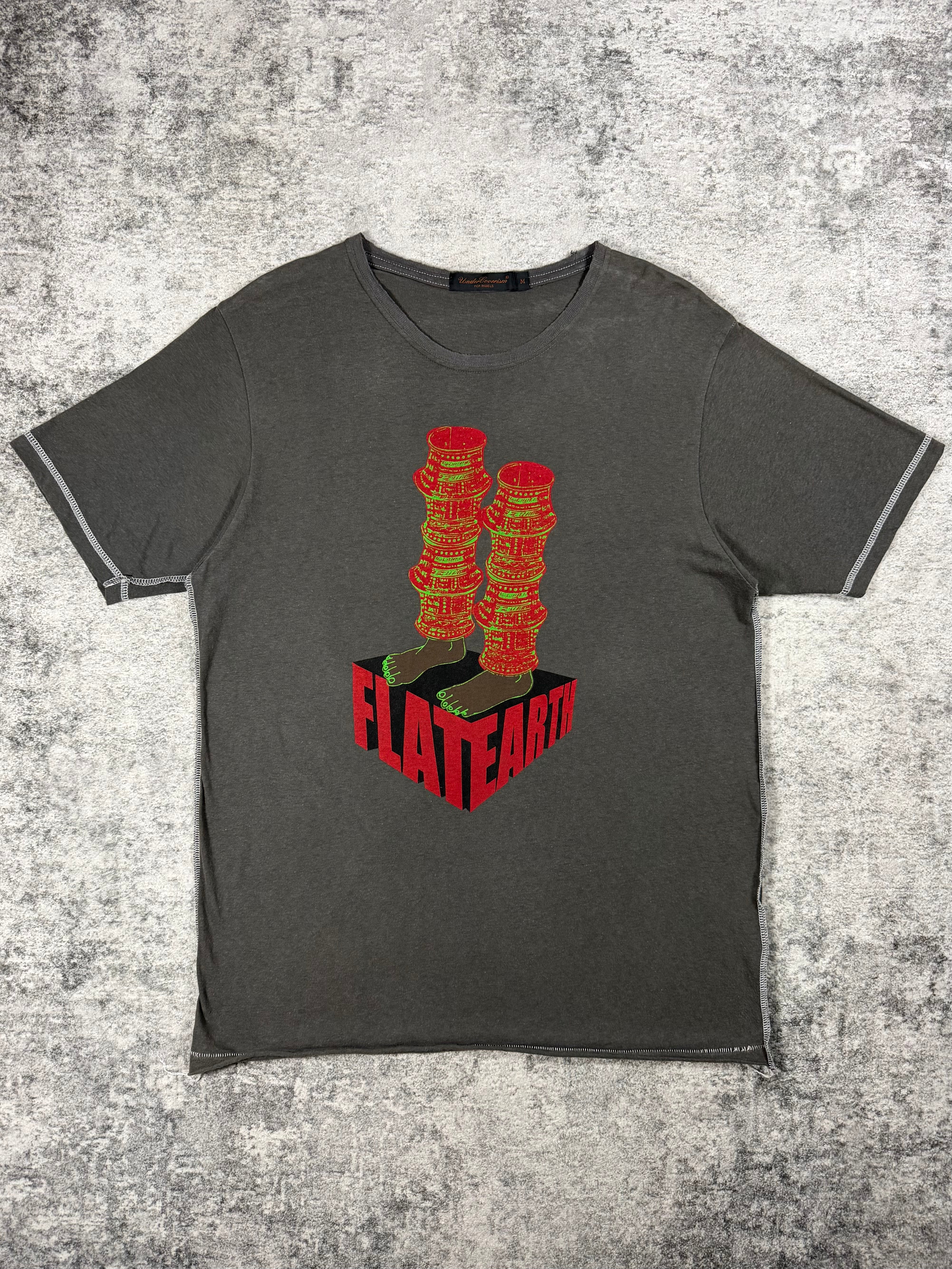 A dark gray Undercover 2003 Scab t shirt with a graphic print of two armored legs red 3D block that reads 'FLATEARTH', laid flat on a textured gray background.