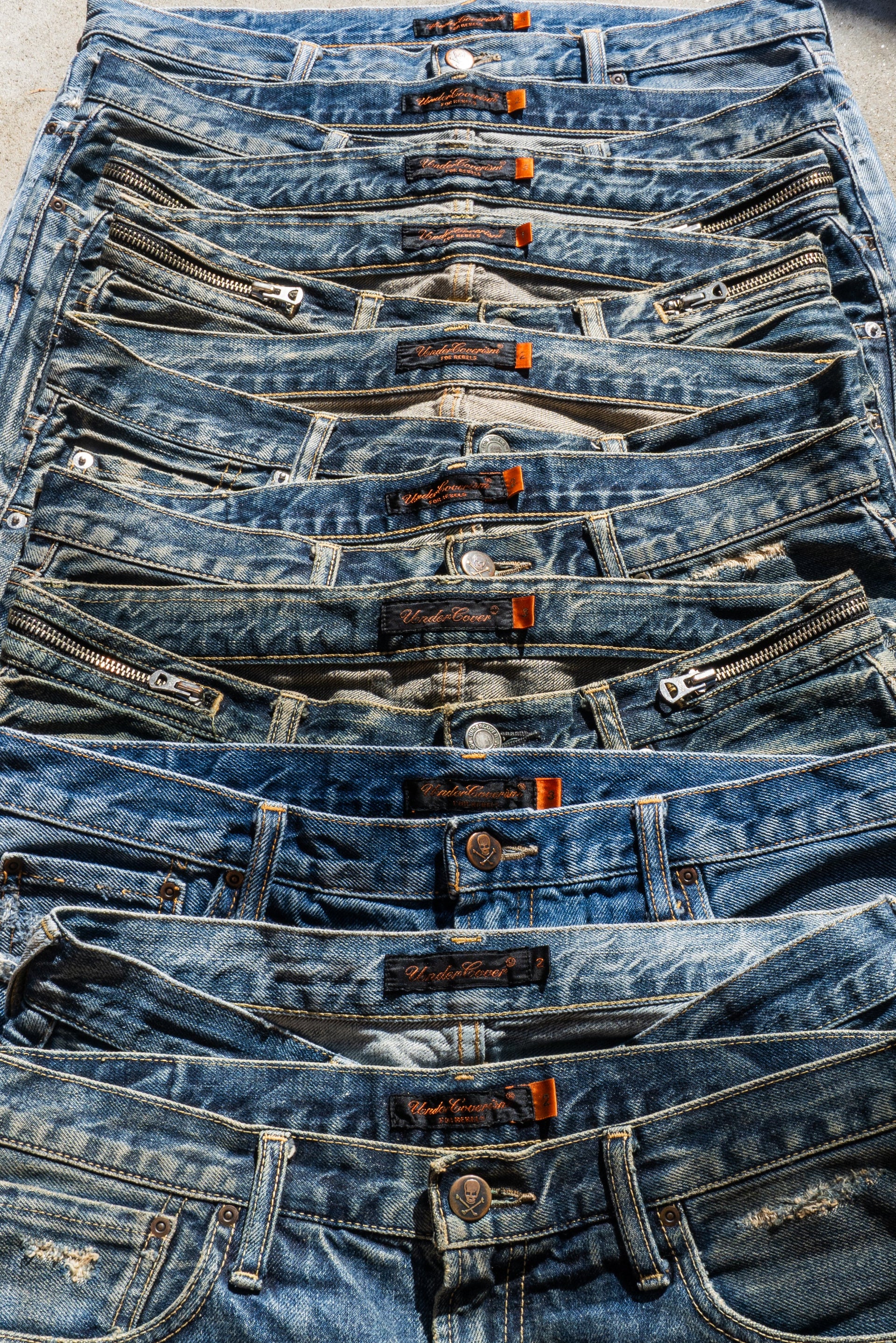 Stack of blue Undercover jeans with visible branding on a neutral background